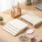 A beige ring binder notebook set arranged on a light wood desk, including a closed binder, lined notepad sheets, washi tape rolls, a cloud-shaped sticky note pad, a pink stapler, and a small plant in a pot.