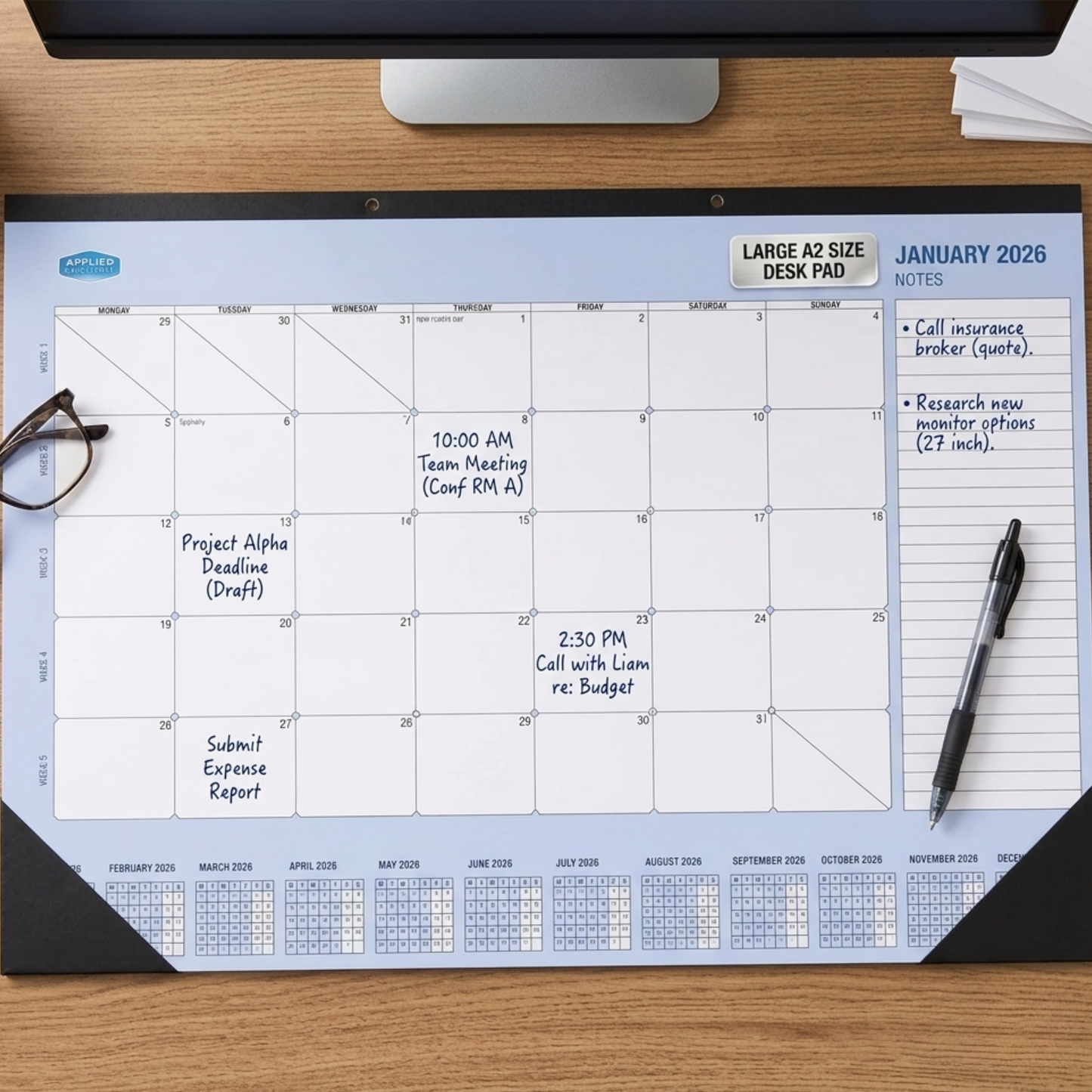 2026 Calendar desk pad on a wooden desk with a pen and glasses