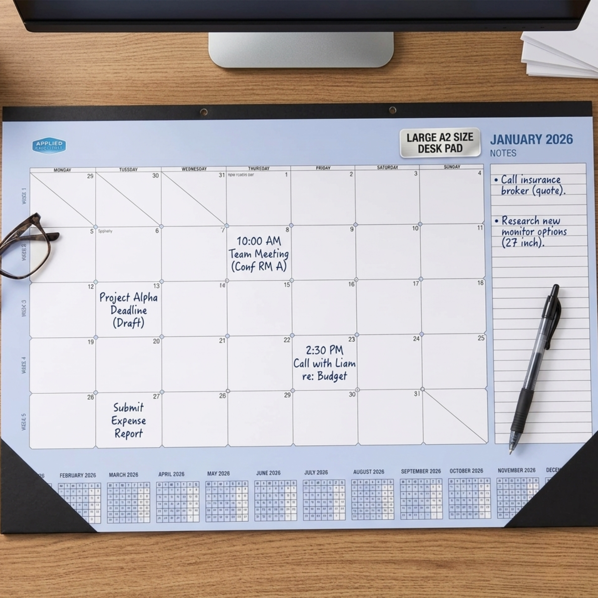 2026 Calendar desk pad on a wooden desk with a pen and glasses