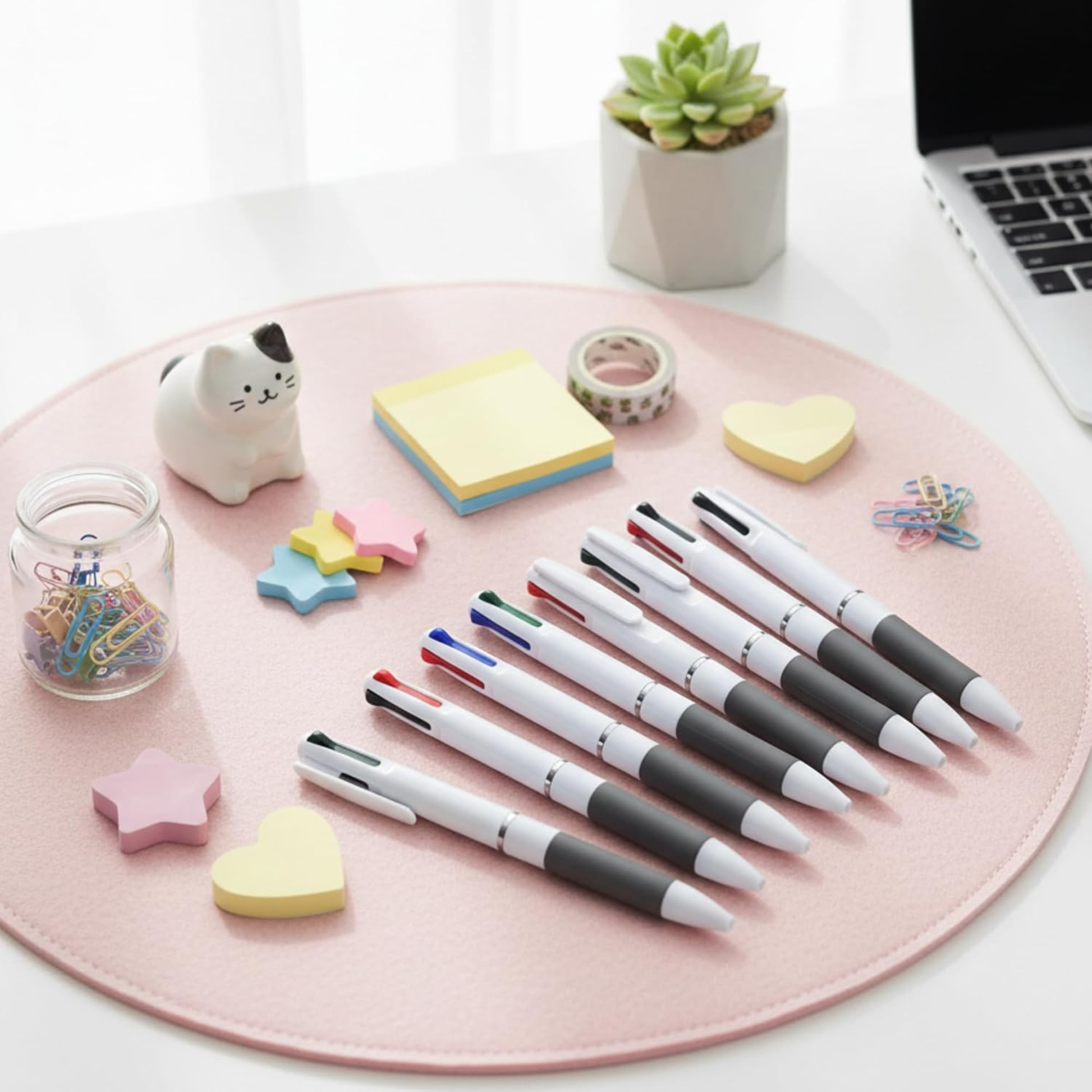 Set of pens on a pink mouse pad with stationery items and a laptop in the background.