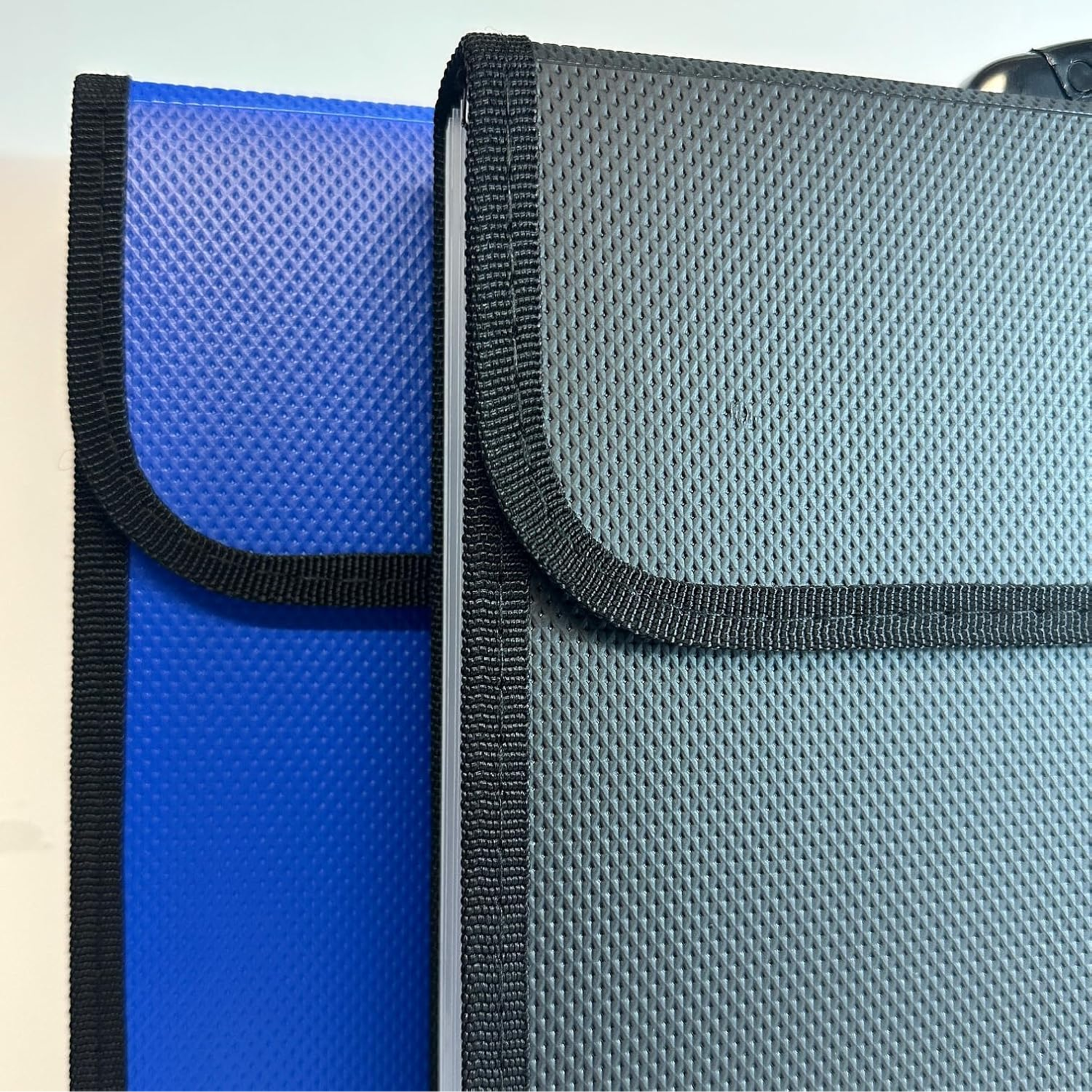 Two textured zippered sleeve or case covers shown close up on a plain light background, one in bright blue and one in dark gray, both with black trim and flap closures.