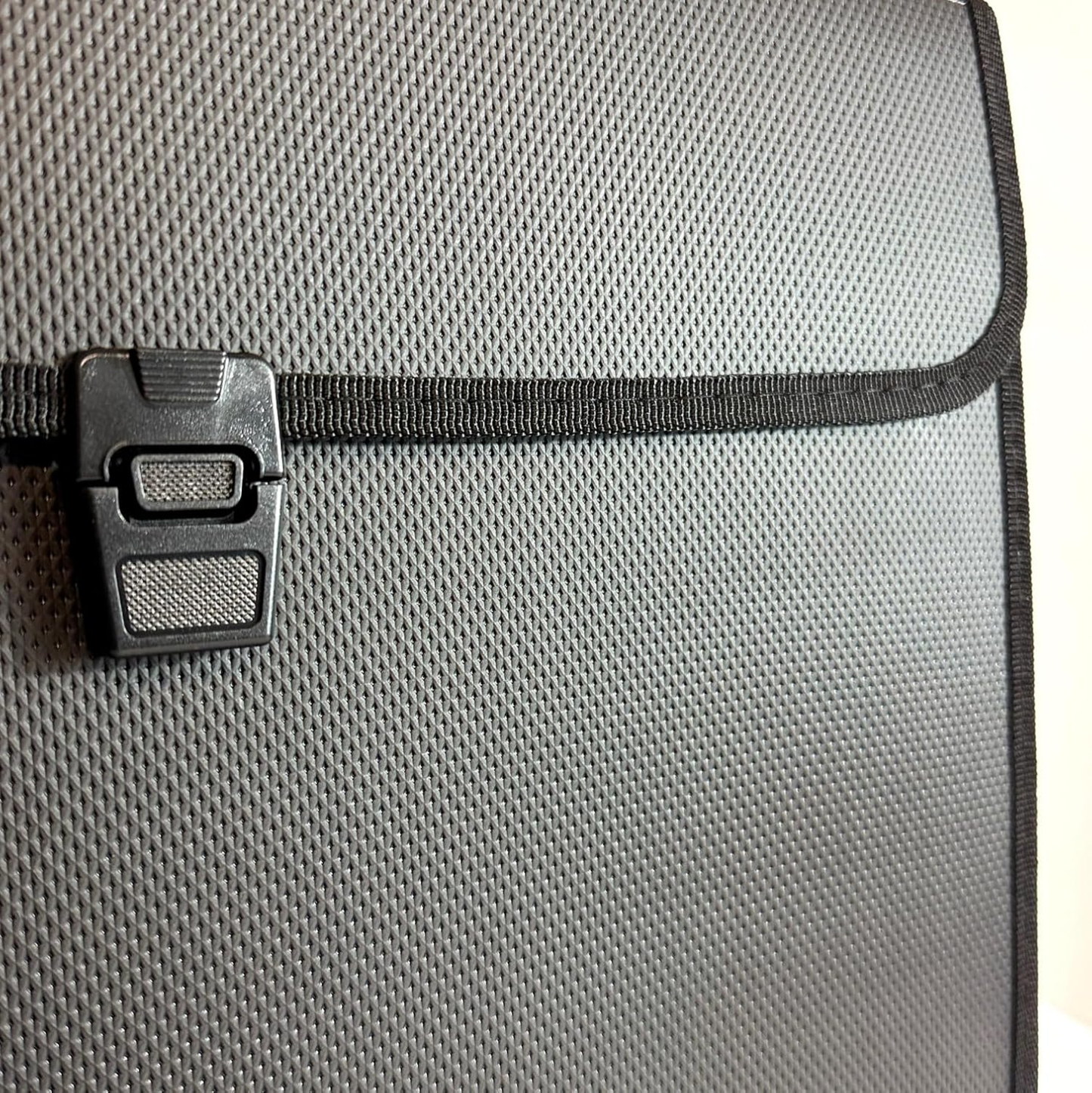 Close-up of a gray textured fabric bag with a black zipper closure and black plastic latch.