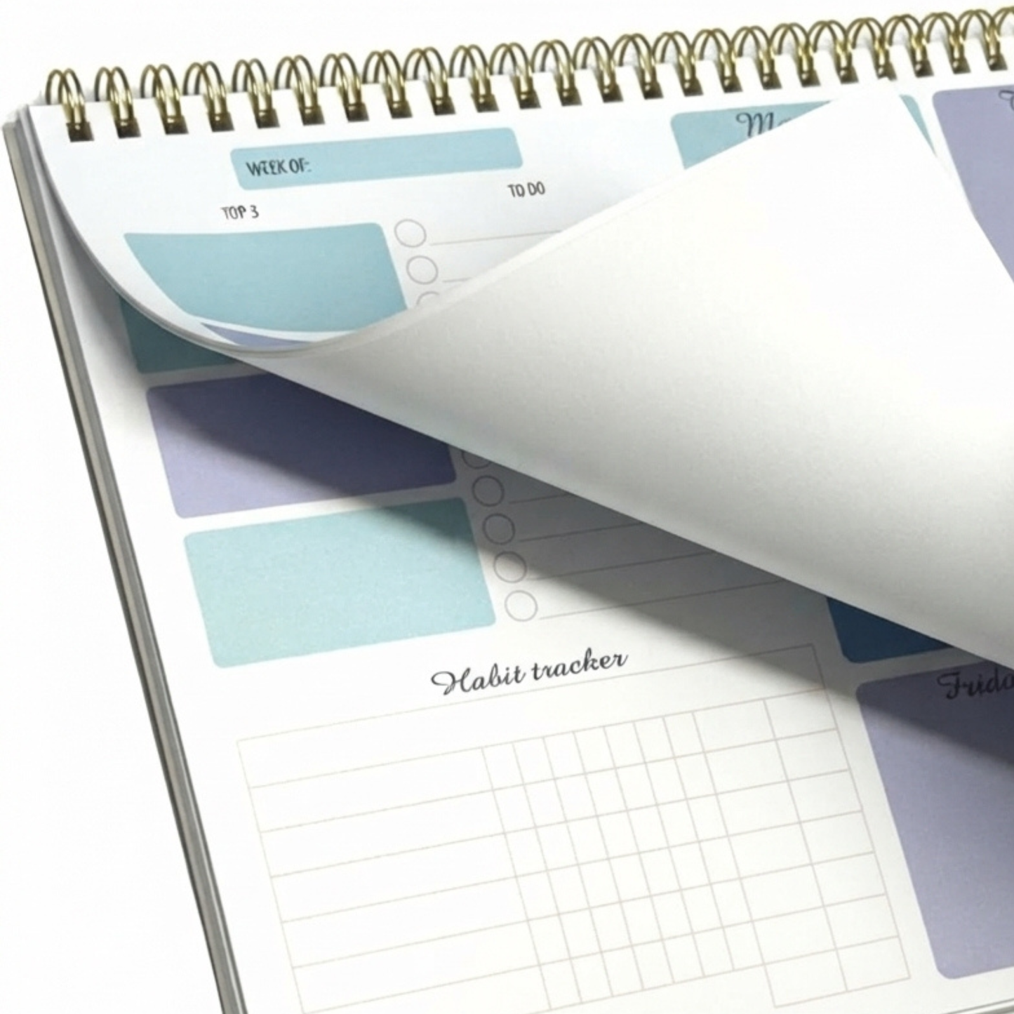 A spiral-bound planner or habit tracker notebook shown open on a white background, with one page curled back to reveal pastel blue and lavender printed sections including a habit tracker grid.